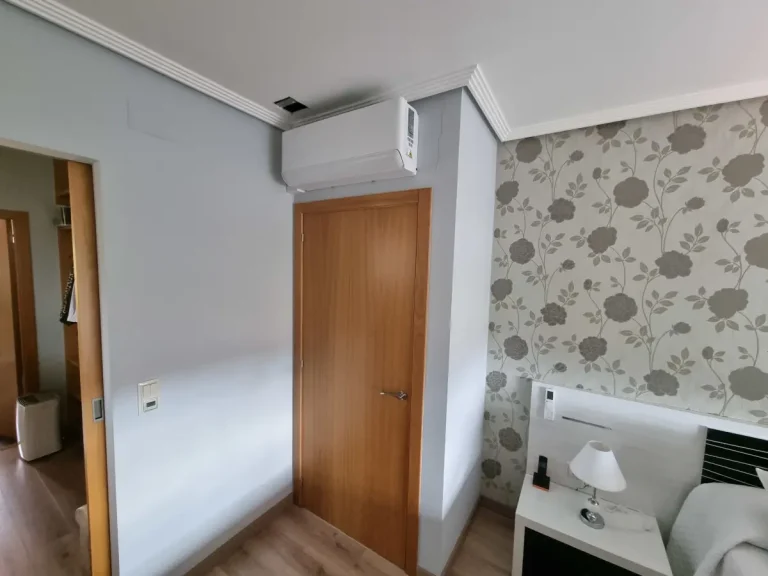 Máquina interior de aire acondicionado sin canaletas a la vista montada sobre la puerta de un dormitorio en Cangas.