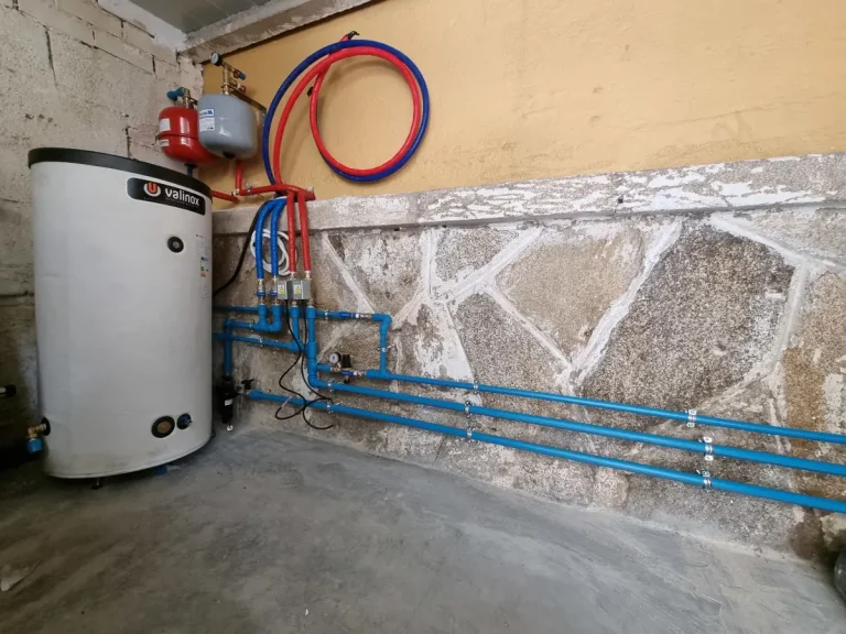 Instalación de Aerotermia en Marín Tuberías y componentes hidráulicos de aerotermia agrupados de forma ordenada en la pared de un garaje en Marín.